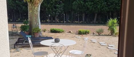 Un patio al aire libre con una mesa redonda y sillas, rodeado de plantas en macetas y un árbol grande.