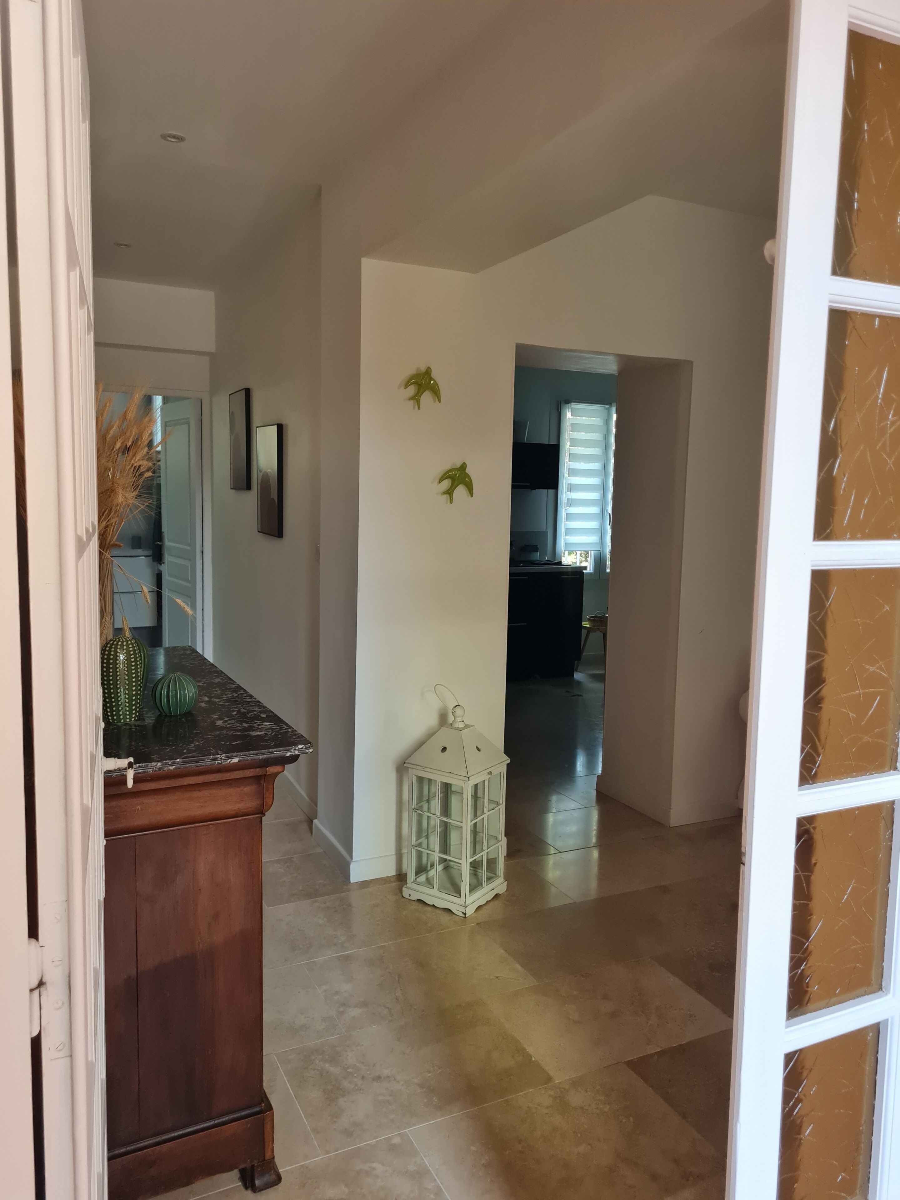A hallway with a wooden cabinet, a white lantern, and a door leading to another room.