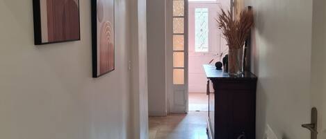 Un couloir avec deux œuvres d’art encadrées accrochées au mur, une porte avec des panneaux en verre dépoli et un radiateur sur la droite.