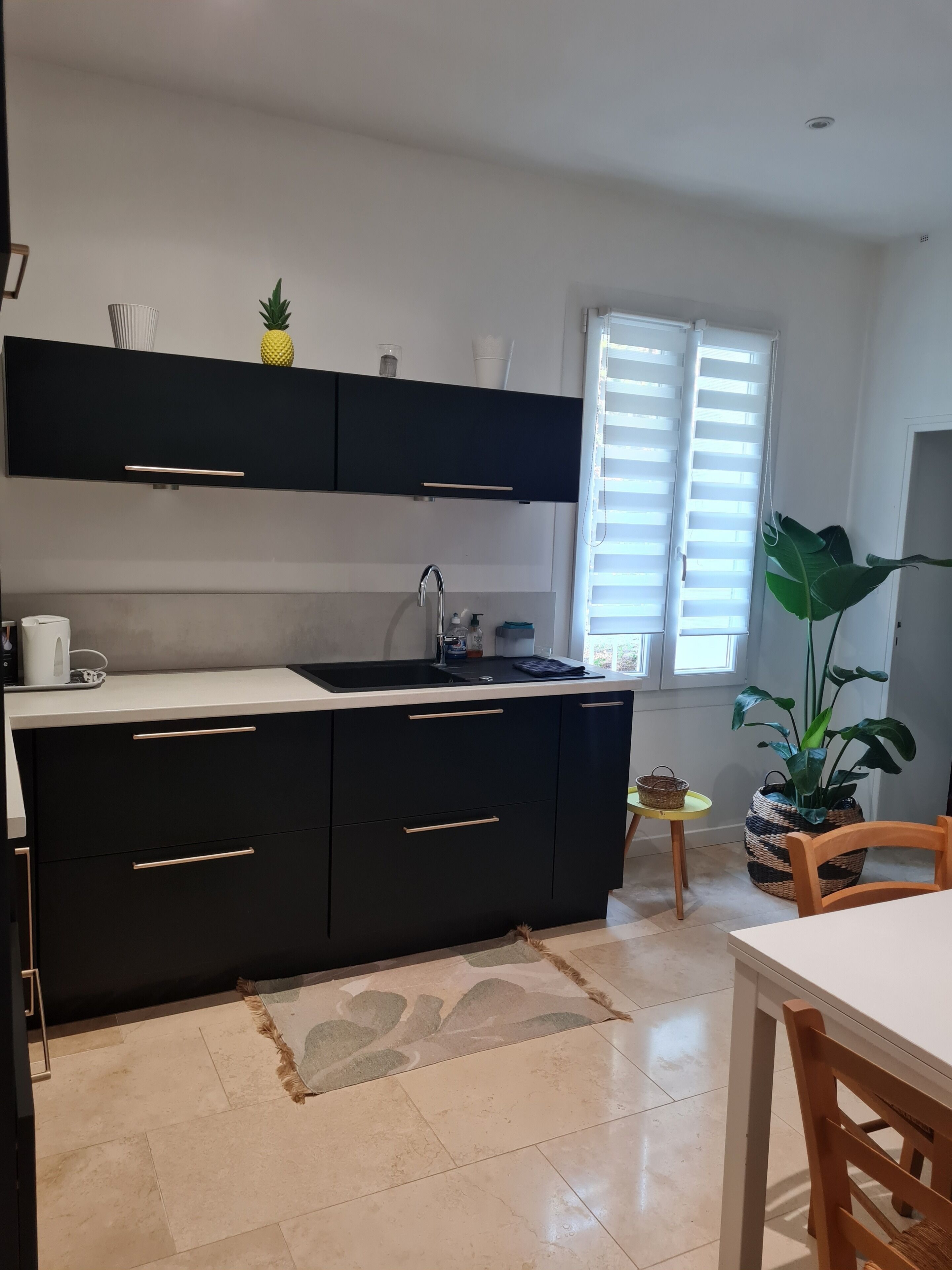A modern kitchen with black cabinets, a white countertop, and a window with blinds.