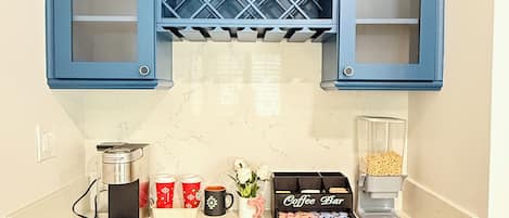 A kitchen with blue cabinets, a coffee maker, mugs, and a coffee bar.