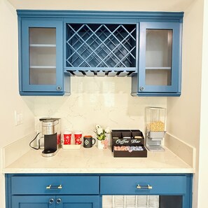 Une cuisine avec des meubles de rangement bleus, une machine à café, des tasses et un coin café.