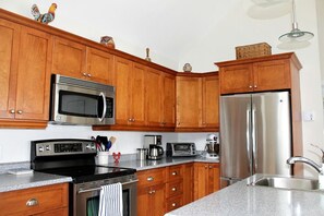 Cozinha com armários de madeira, eletrodomésticos de aço inoxidável, incluindo micro-ondas, forno e geladeira, e bancada de granito.