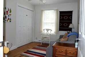 A room with a bed, a dresser, a chair, a window with curtains, and a wall with a patterned tapestry. - Romantic Waterfront Cottage with Private Beach & Fireplace Near Hancock, Maine (Hancock)