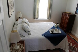 A neatly arranged bedroom with a bed, bedside lamp, a tray with cups and a vase of flowers, and a dresser. - Romantic Waterfront Cottage with Private Beach & Fireplace Near Hancock, Maine (Hancock)
