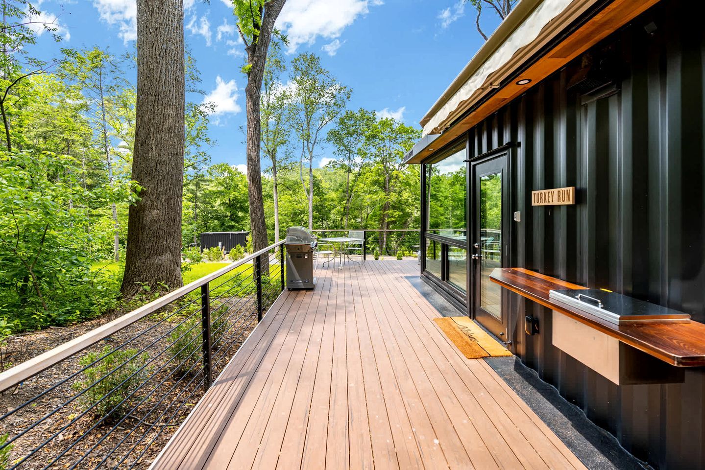 A wooden deck with a grill, a bench, and a sign reading 'TURKEY RUN' on a building.