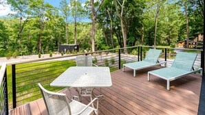 Een terras met een tafel, stoelen en twee lounge fauteuils, met uitzicht op een bebost gebied.