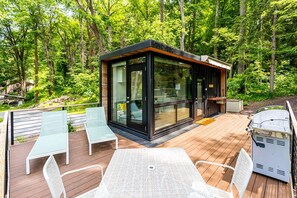 Eine moderne Terrassenanlage im Freien mit Glaswänden, Holzboden und Gartenmöbeln.