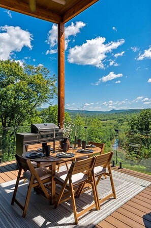 An outdoor dining area with a grill, wooden table, and chairs, overlooking a scenic landscape. - Luxurious Modern Mountain Retreat with Hot Tub & Stargazing Dome Near Berkeley Springs, Hedgesville WV (Hedgesville)