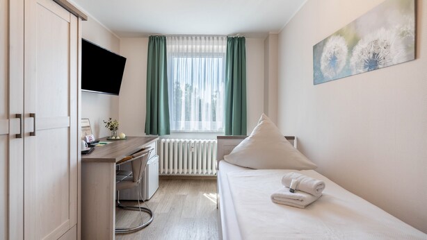 Ein Hotelzimmer mit Bett, Schreibtisch, Fernseher, Heizkörper und einem Fenster mit Vorhängen.