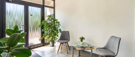 Un balcon moderne avec une porte vitrée, deux chaises grises, une petite table ronde ornée d’un vase et une plante en pot.