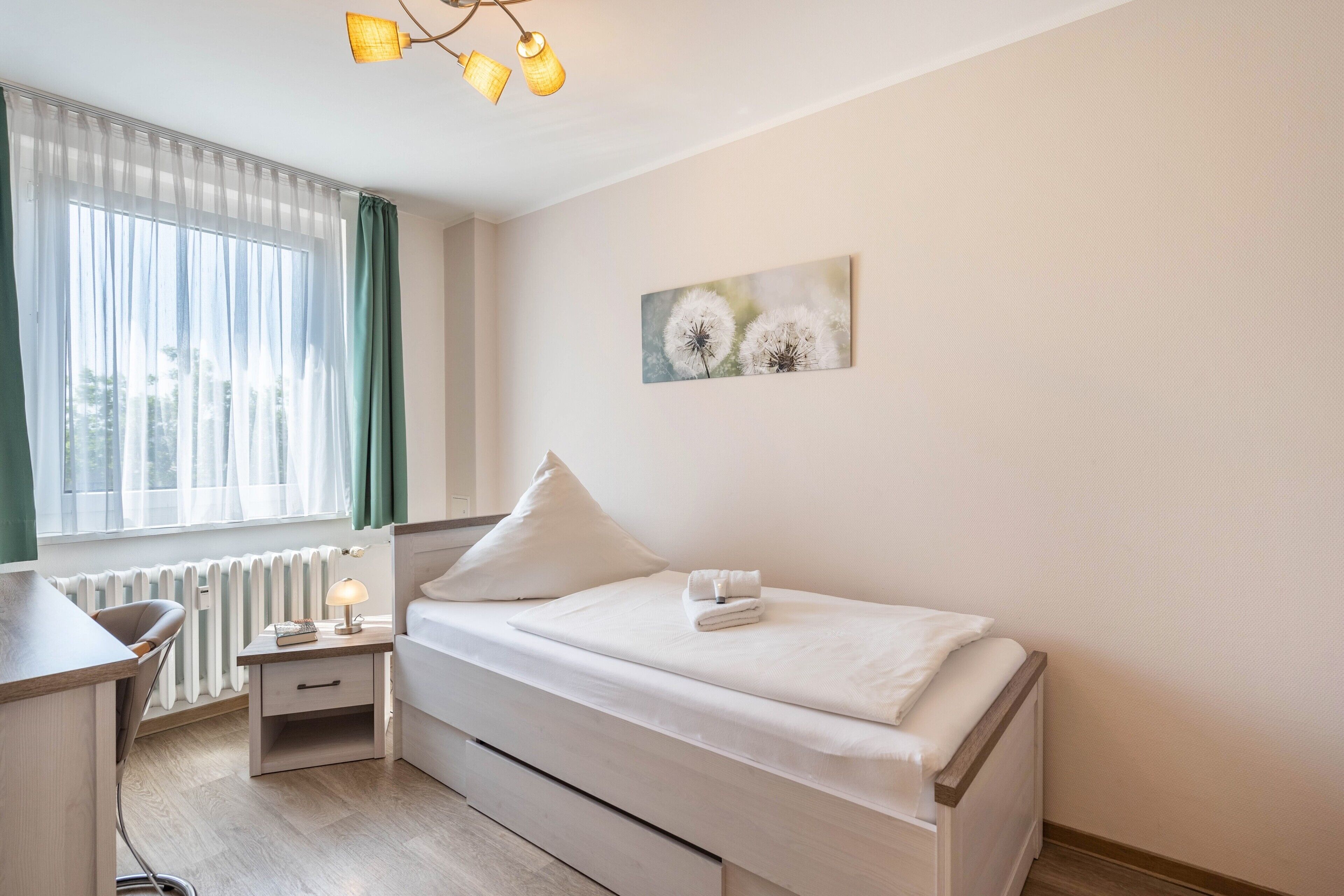 A neatly arranged bedroom with a bed, bedside table, lamp, and a window with curtains.