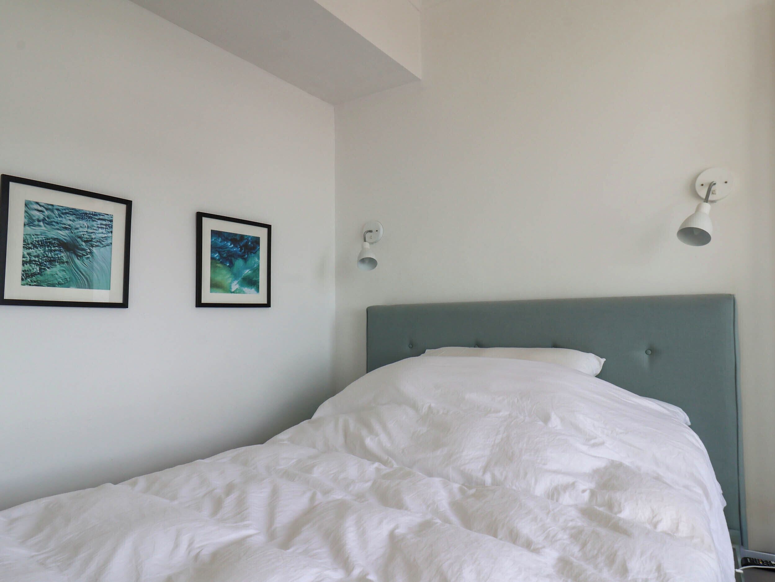 Un dormitorio con cama, dos cuadros en la pared y una lámpara.