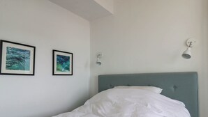 Ein Schlafzimmer mit einem Bett, zwei gerahmten Bildern an der Wand und einer Deckenleuchte.