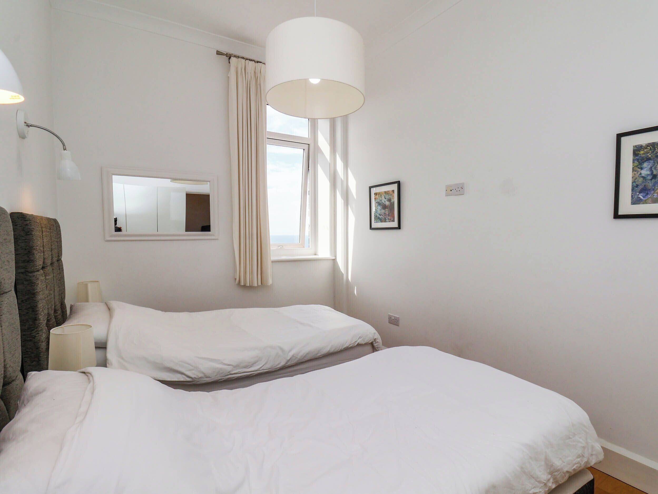 Une chambre avec deux lits, une fenêtre avec des rideaux, un miroir et un luminaire fixé au mur.
