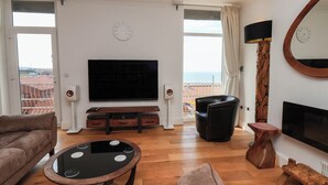 Ein Wohnzimmer mit Flachbildfernseher, zwei Sofas, einem Couchtisch und einem Balkon mit Meerblick.