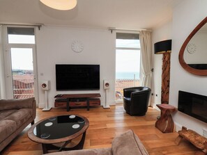 Ein Wohnzimmer mit Flachbildfernseher, zwei Sofas, einem Couchtisch und einem Balkon mit Meerblick.