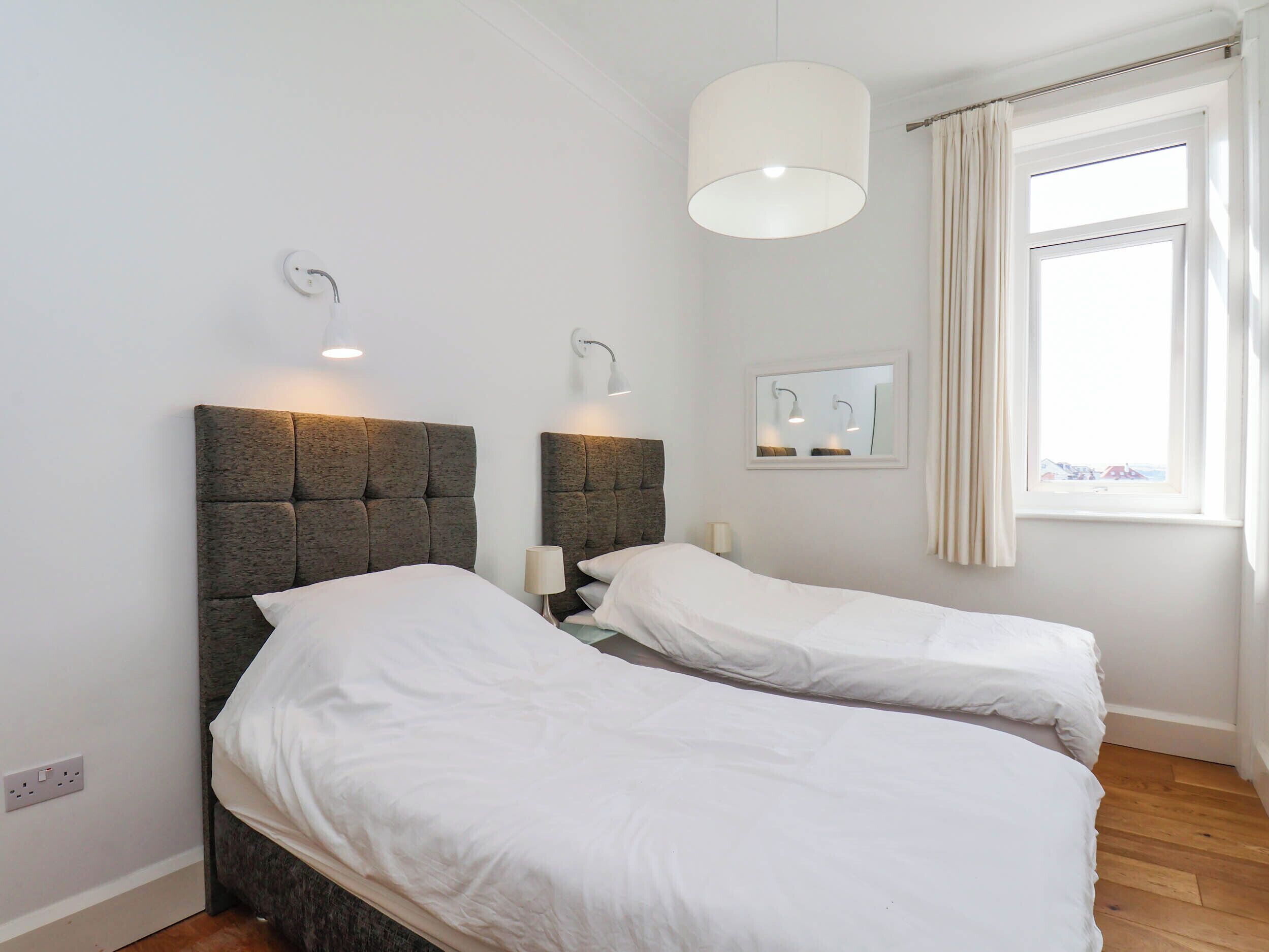 Een kamer met twee bedden, een raam met gordijnen en wandlampen.