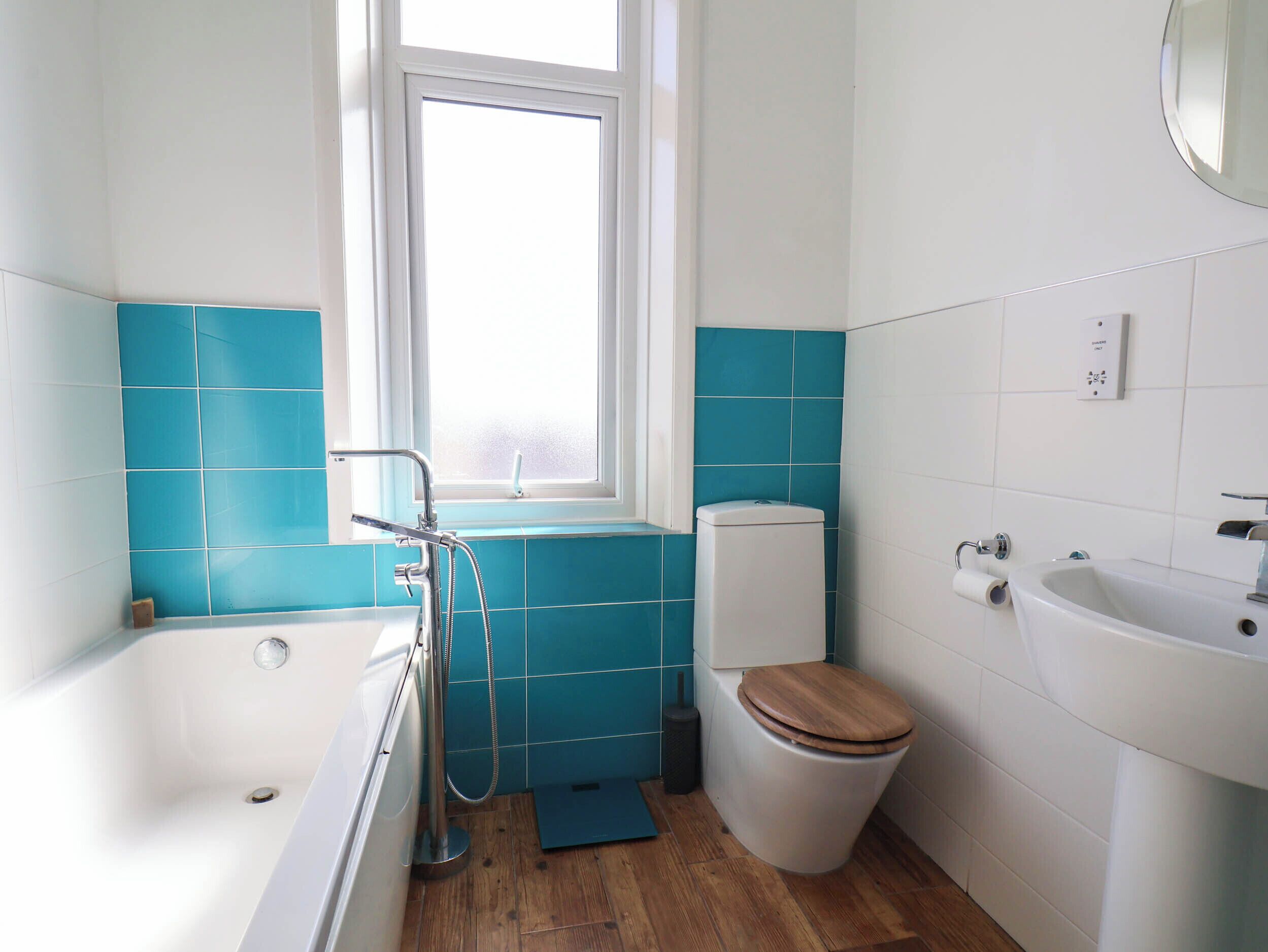 Ein Badezimmer mit Badewanne, Toilette und Waschbecken, mit blauen Fliesen und Holzboden.