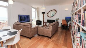A modern living room with a sofa set, a dining table with chairs, a bookshelf, a flat-screen TV, and a large mirror.
