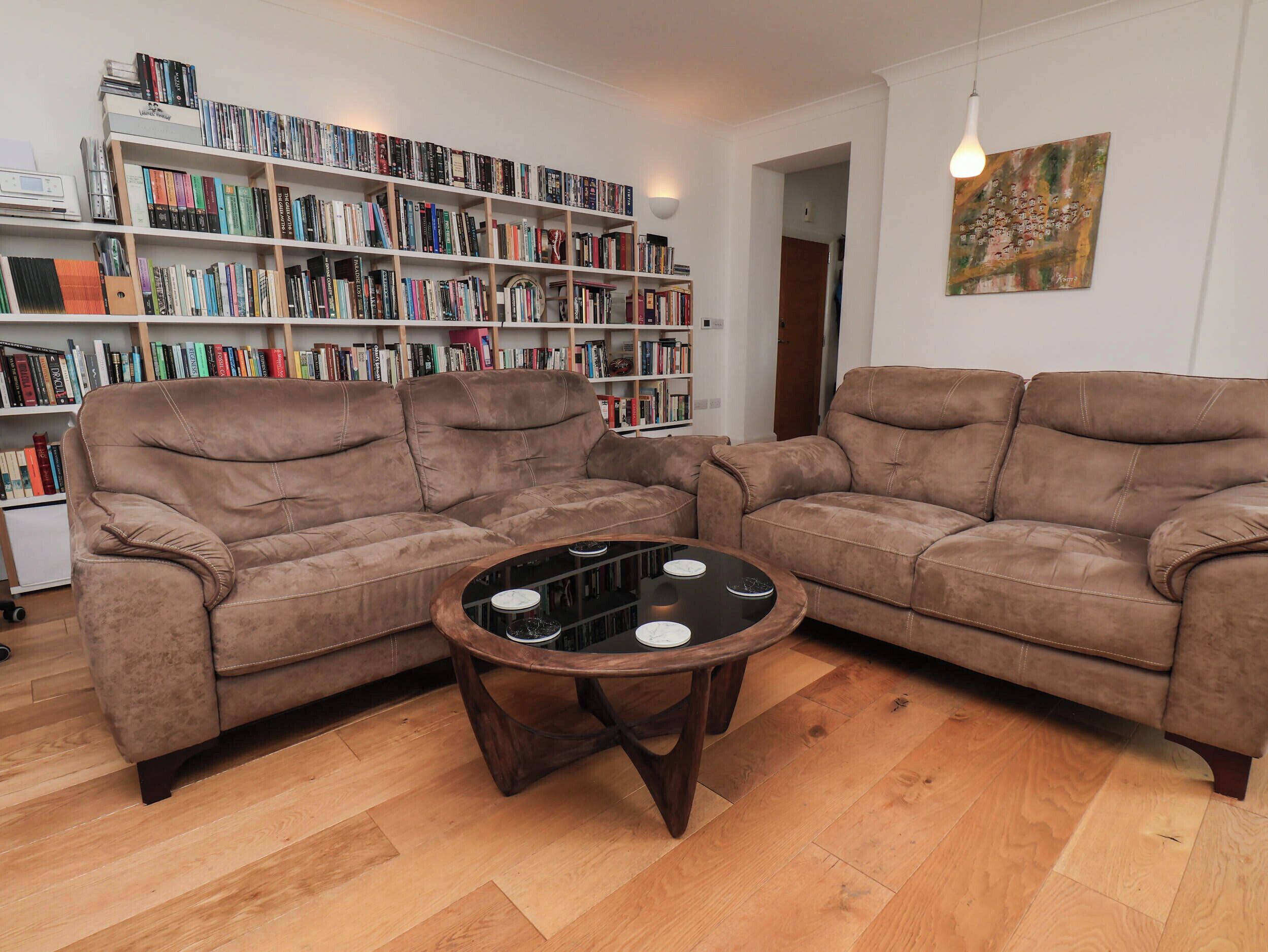 A living room with two brown sofas, a coffee table, and a bookshelf filled with books.