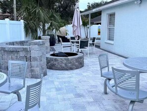 Un patio al aire libre con fogón de piedra, asientos, mesas y sillas.