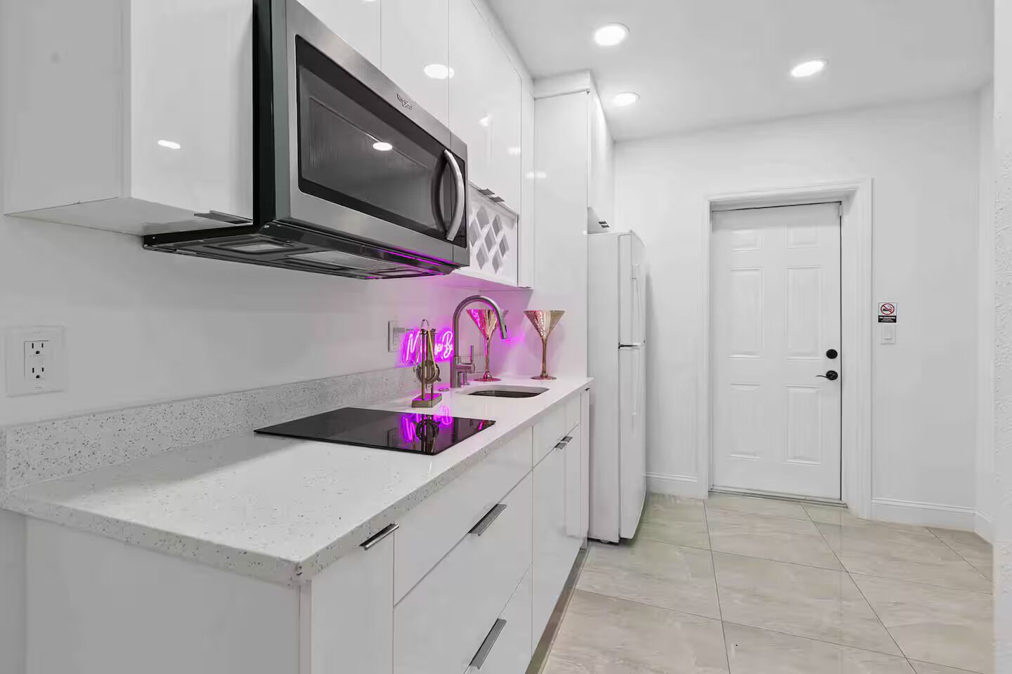 A modern kitchen with white cabinets, a black induction cooktop, a microwave, and a stainless steel refrigerator.