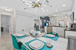 Une cuisine moderne dotée d’un îlot central, d’appareils électroménagers en acier inoxydable et d’un coin repas avec une table blanche dressée pour quatre personnes.