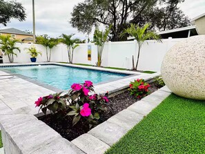 A swimming pool with a stone border, surrounded by a white fence, and a large rock on the right. - Luxury Home/Heated Pool/TPA Airport/Disney (Tampa)