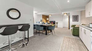 Une cuisine moderne avec des meubles blancs, un coin repas comprenant une table et des chaises, et un petit coin bar avec des tabourets.