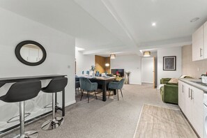 A modern kitchen with white cabinets, a dining area with a table and chairs, and a small bar area with stools. - Modern Leeds Flat | Ideal for Work & Stay (Leeds)