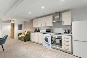 A compact kitchen with a washing machine, a microwave, and a built-in oven. - Modern Leeds Flat | Ideal for Work & Stay (Leeds)
