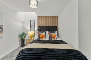 A bedroom with a bed, bedside table, lamp, and a potted plant. - Modern Leeds Flat | Ideal for Work & Stay (Leeds)