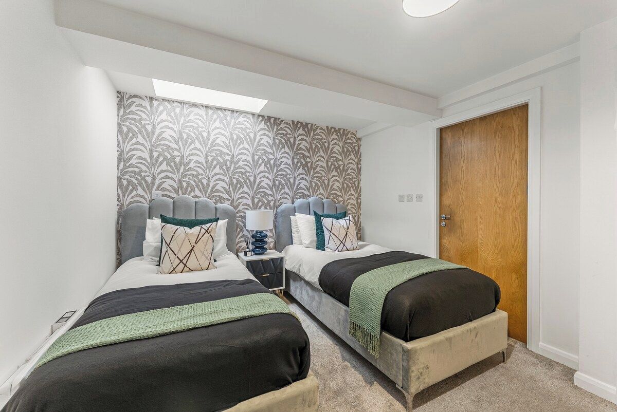 Une chambre avec deux lits, une porte en bois et un papier peint à motifs.