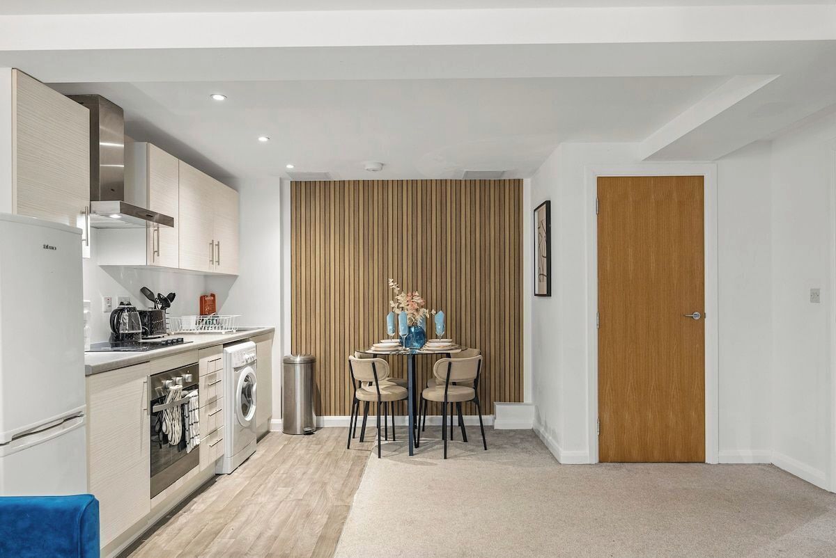 A compact kitchen with modern appliances, a dining area with a table and chairs, and a wooden panel wall.