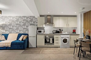 A compact living space with a kitchenette, a washing machine, a dining area, and a sofa. - Modern Leeds Flat | Ideal for Work & Stay (Leeds)