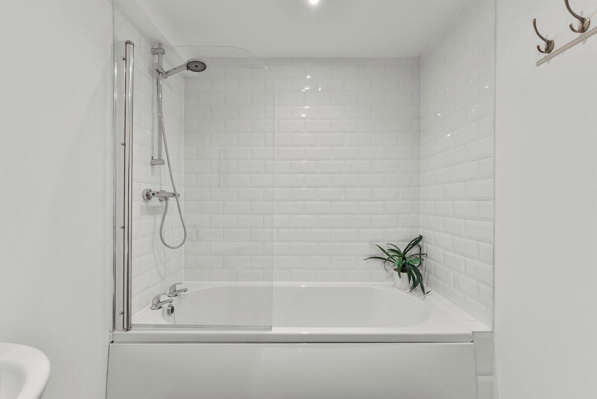 Een moderne badkamer met een douchecabine van glas, een witte badkuip en een kleine potplant.
