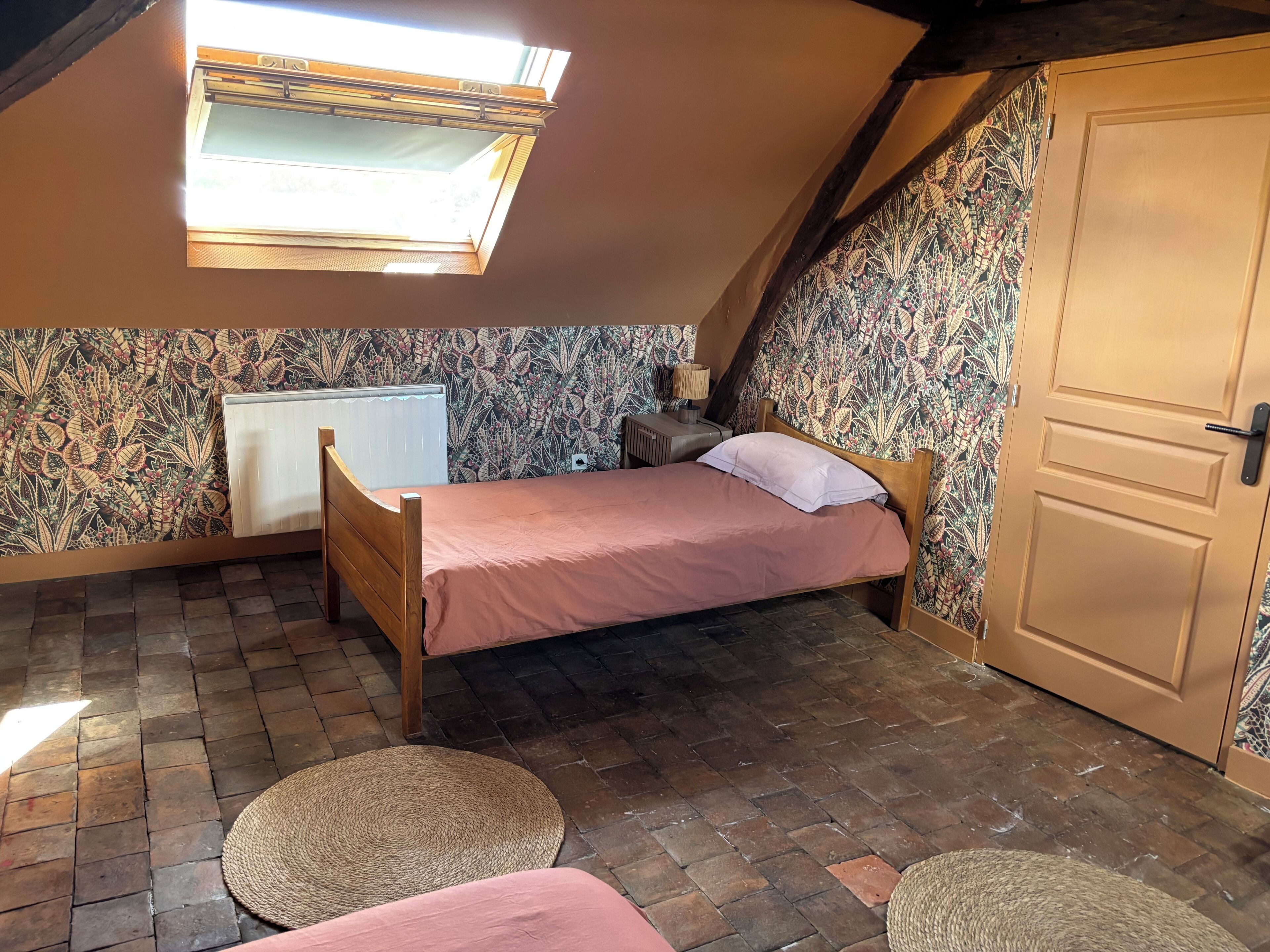A bedroom with a sloped ceiling, a bed, a radiator, a door, and a window.