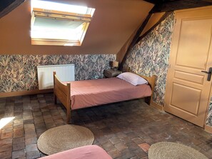 A bedroom with a sloped ceiling, a bed, a radiator, a door, and a window. - Fully Furnished and Renovated Apartment (Vitry-aux-Loges)