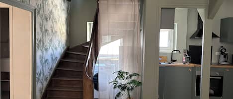 A staircase leading to a second floor, a kitchen area with modern appliances, and a potted plant.