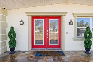 A red double door with a glass panel, flanked by two black lantern-style lights, and a welcome mat with a blue design. - Gorgeous Home/Heated Pool/Clearwater/Tampa/Disney (Tampa)
