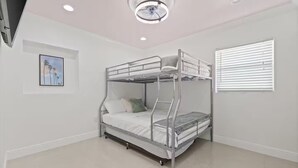 Een stapelbed in een kamer met witte muren, een plafondlamp en een raam met zonwering.