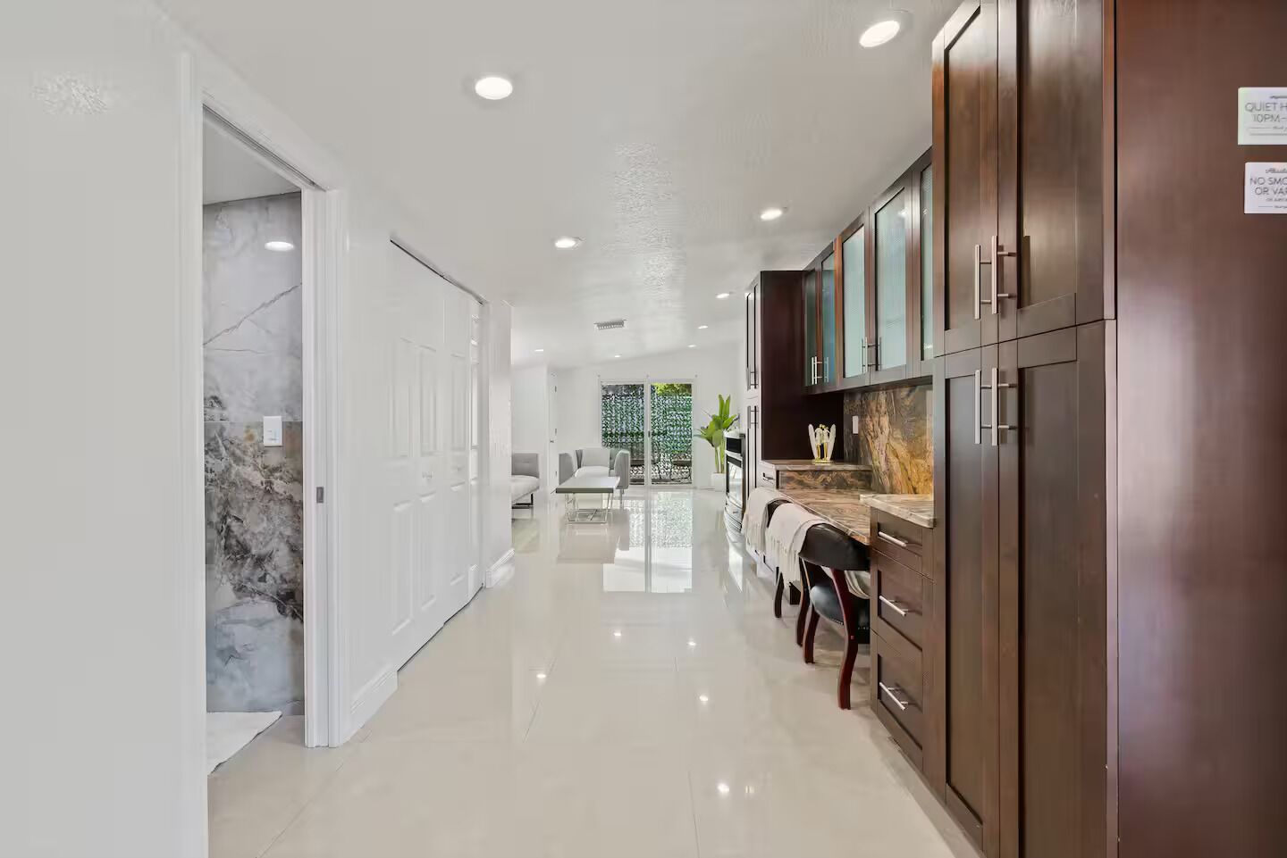 A modern kitchen with dark wood cabinets, a marble countertop, and a dining area with a white table and chairs.