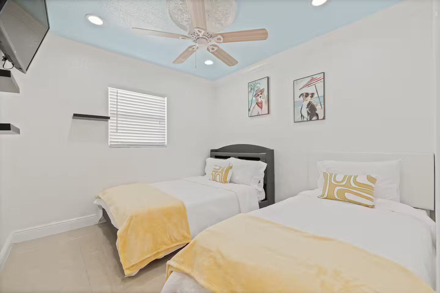 A bedroom with two beds, a ceiling fan, and artwork on the walls.