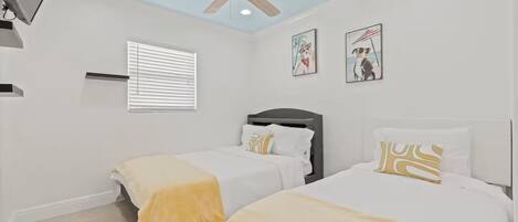 A bedroom with two beds, a ceiling fan, and artwork on the walls.