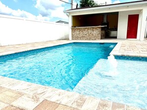 Ein rechteckiger Pool mit Steinrand und einer Terrassenfläche mit einer roten Tür.