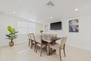 A dining area with a wooden table and chairs, a potted plant, and a flat-screen TV on the wall. - Gorgeous Home/Heated Pool/Clearwater/Tampa/Disney (Tampa)