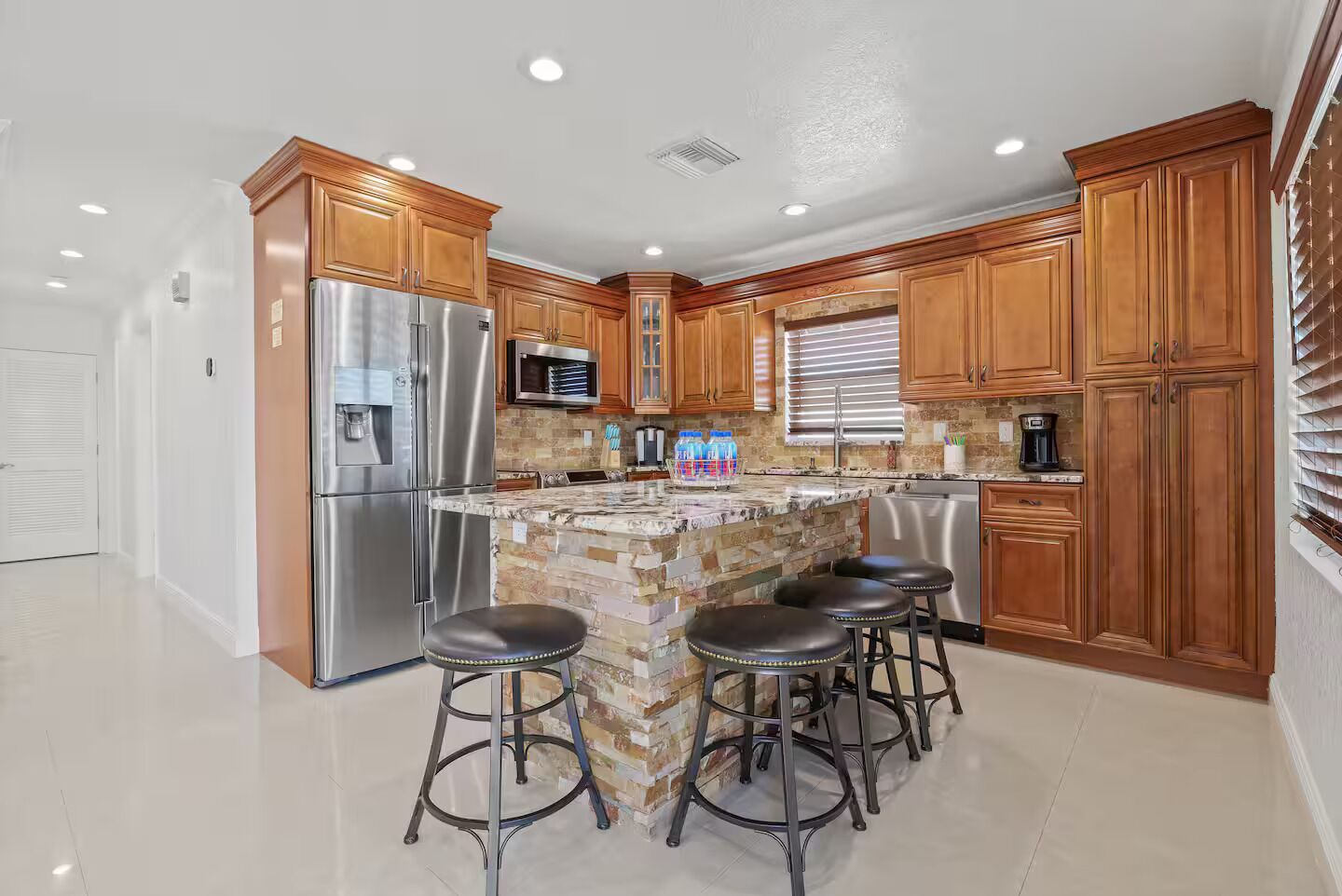 A kitchen with wooden cabinets, stainless steel appliances, a granite countertop, and a bar stool area.