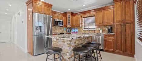 A kitchen with wooden cabinets, stainless steel appliances, a granite countertop, and a bar stool area.