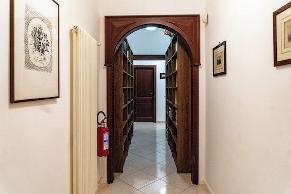A hallway with a fire extinguisher, framed pictures on the walls, and a tiled floor.